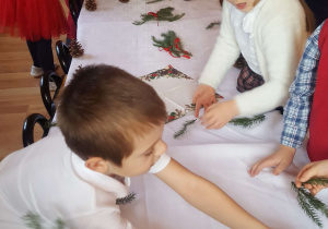 Przedszkolaki ozdabiają gałązkami świąteczny stół.